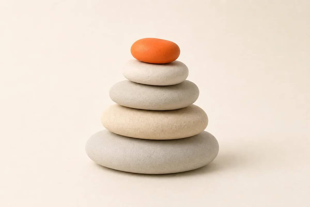 Five smooth pebbles stacked large to small, the top one orange.